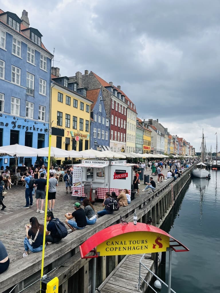 Colorful historic houses lining Nyhavn harbor in Copenhagen, with boats and tourists strolling along the waterfront.