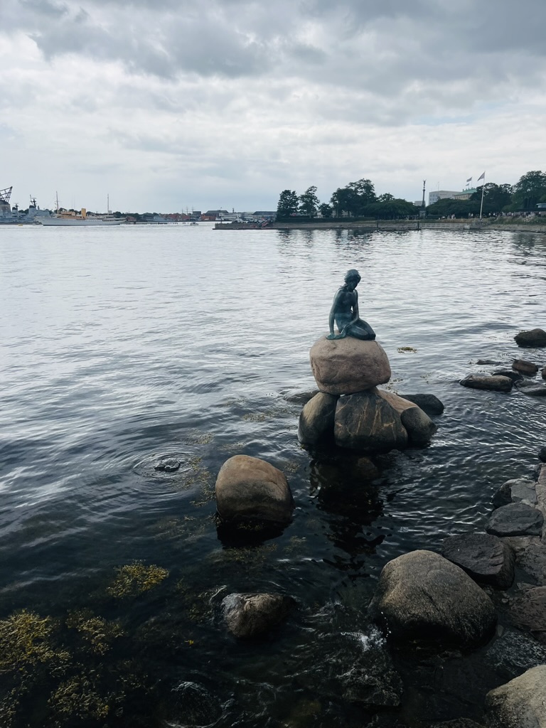 The Little Mermaid statue in Copenhagen near Kastellet fortress, with visitors photographing the iconic sculpture.